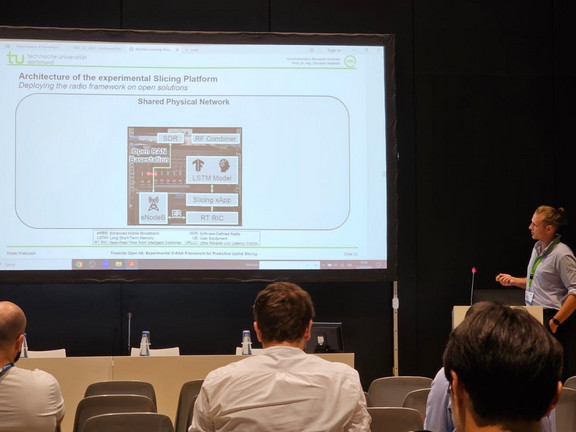 A research assistant presenting slides in front of a plenum