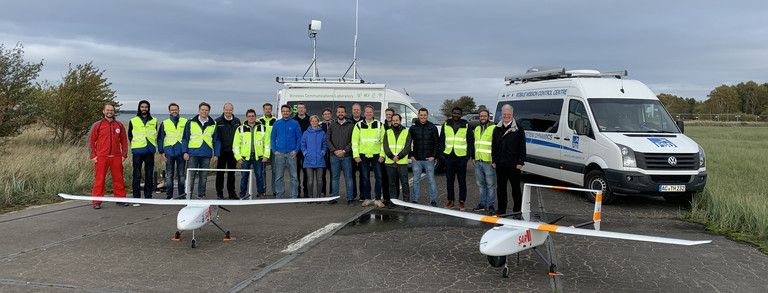Persons standing with two drones in front of them